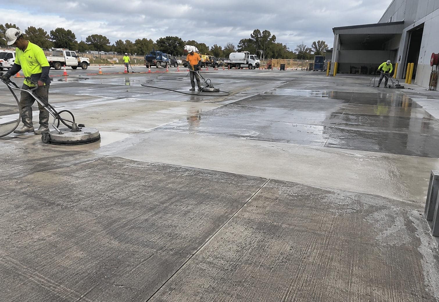 Workers pressure-cleaning a large commercial concrete hardstand with surface cleaners outside a Canberra warehouse