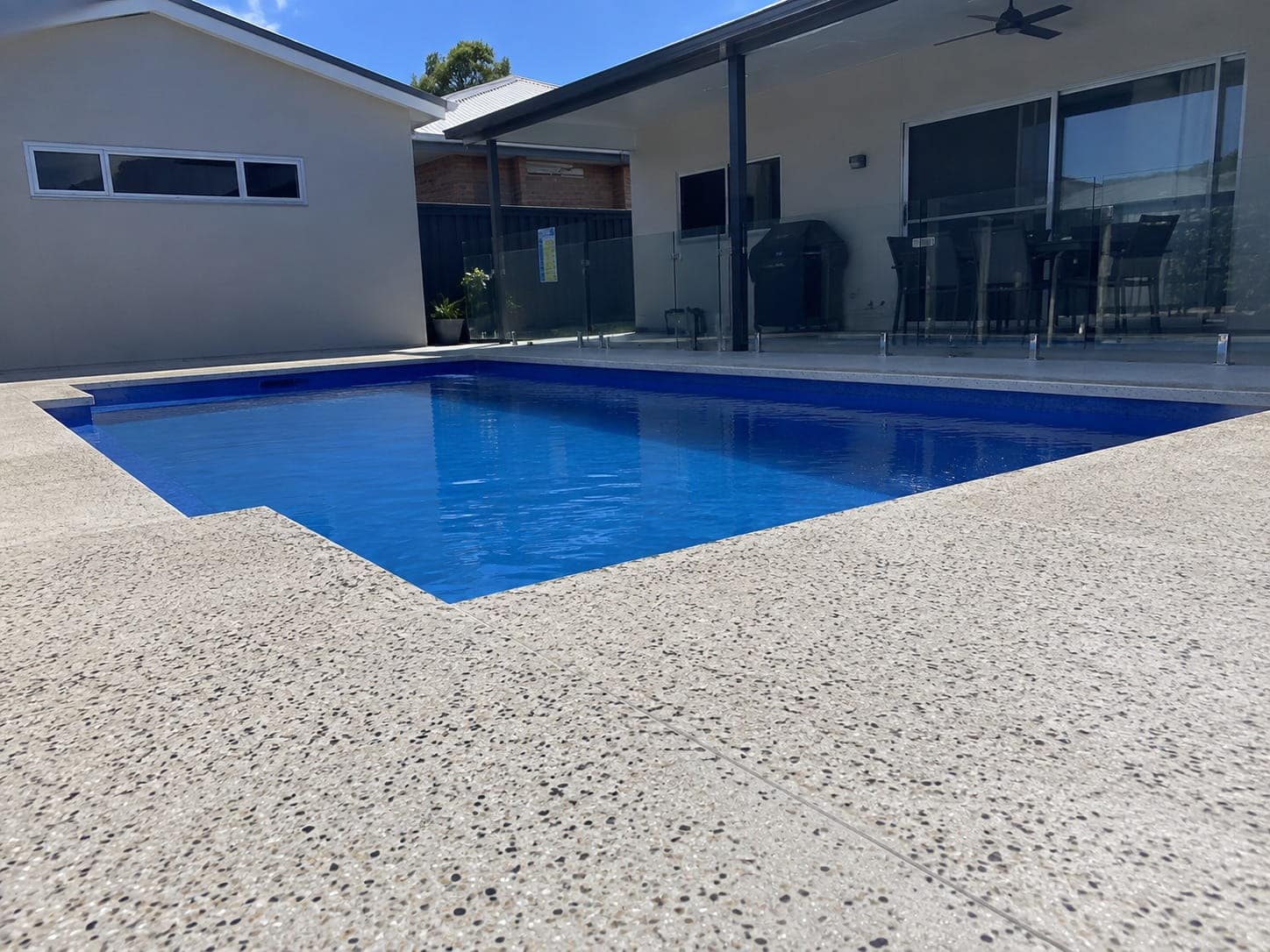Exposed aggregate pool surround beside a blue pool