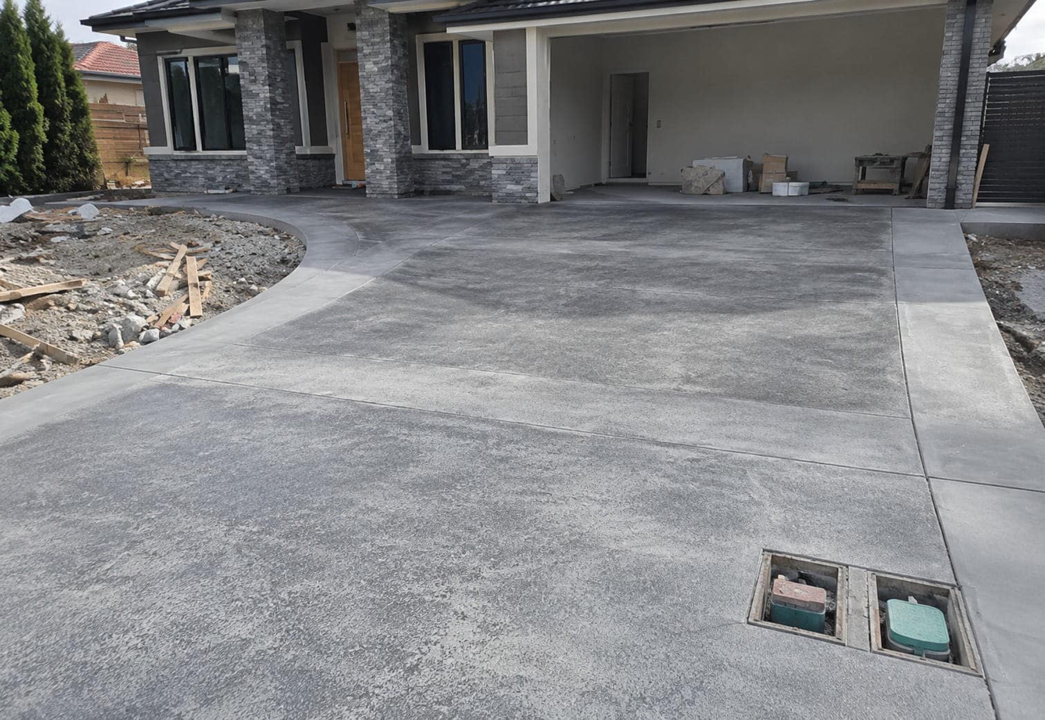 Newly replaced charcoal concrete driveway with saw-cut joints and service pits in front of a Canberra home
