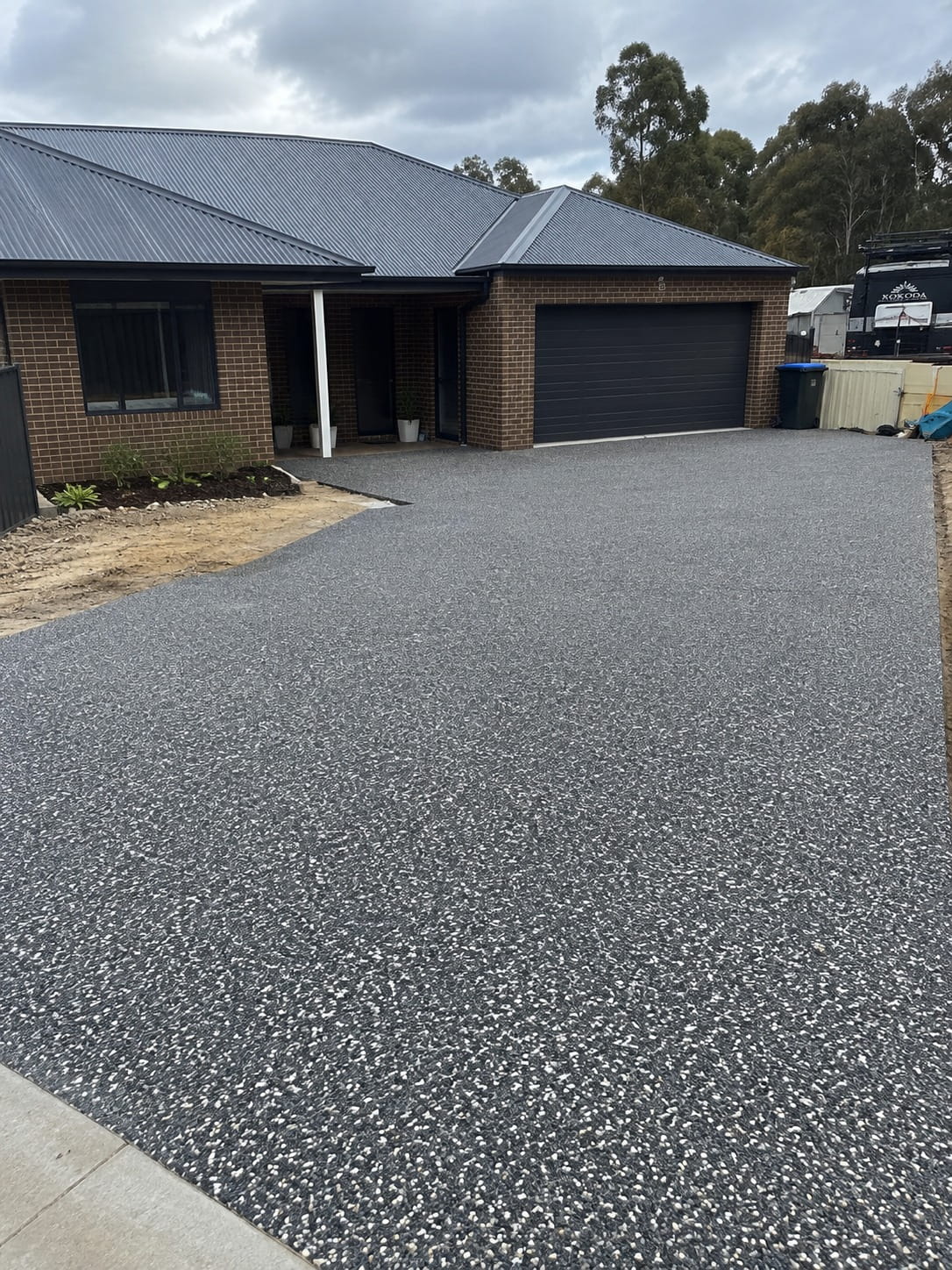 Charcoal exposed aggregate driveway at a Canberra home, finished up to the garage door